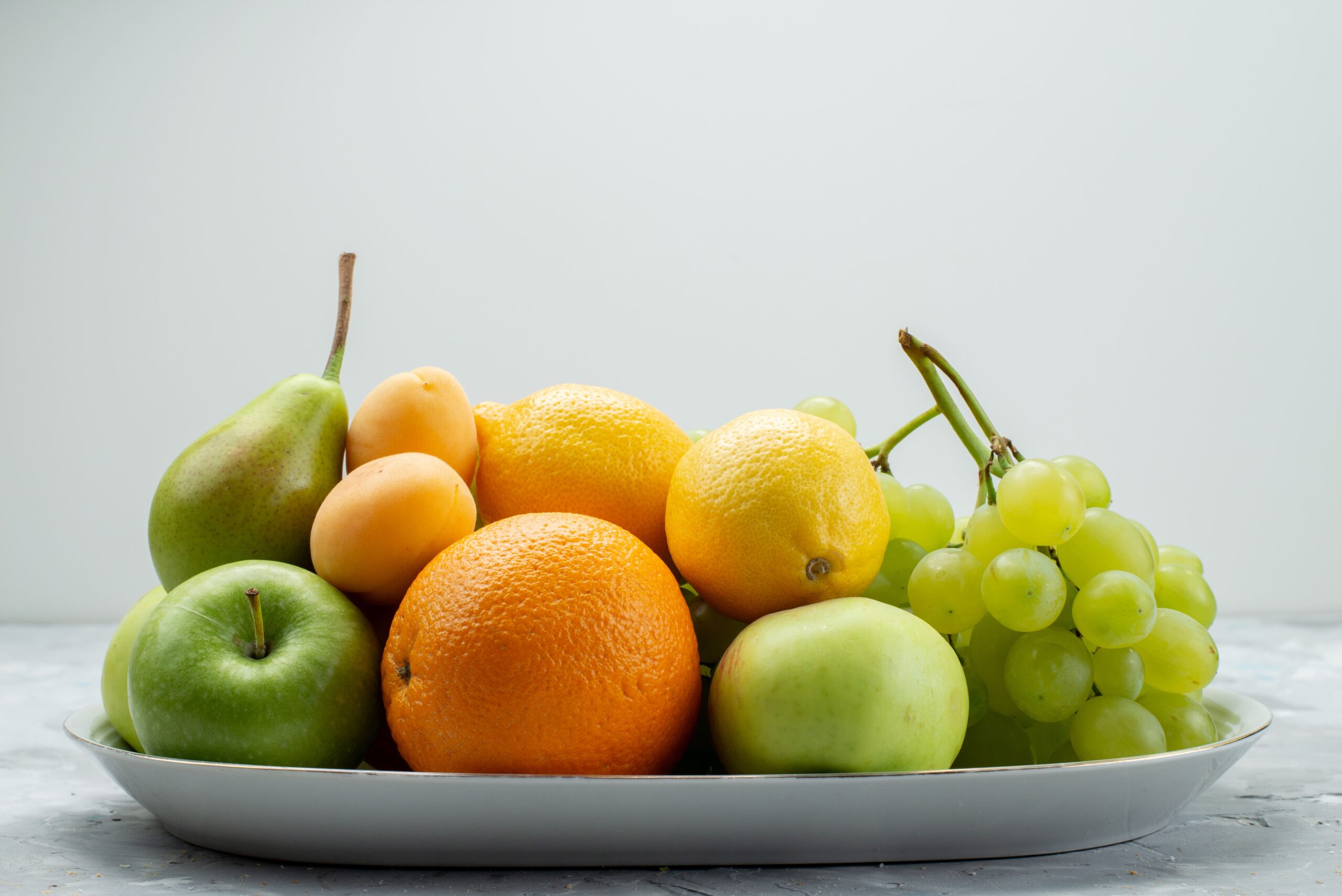 front-view-different-fruits-such-as-lemons-pears-apples-grapes-oranges-white-desk-inside-plate-fruit-color-vitamine-summer-fresh